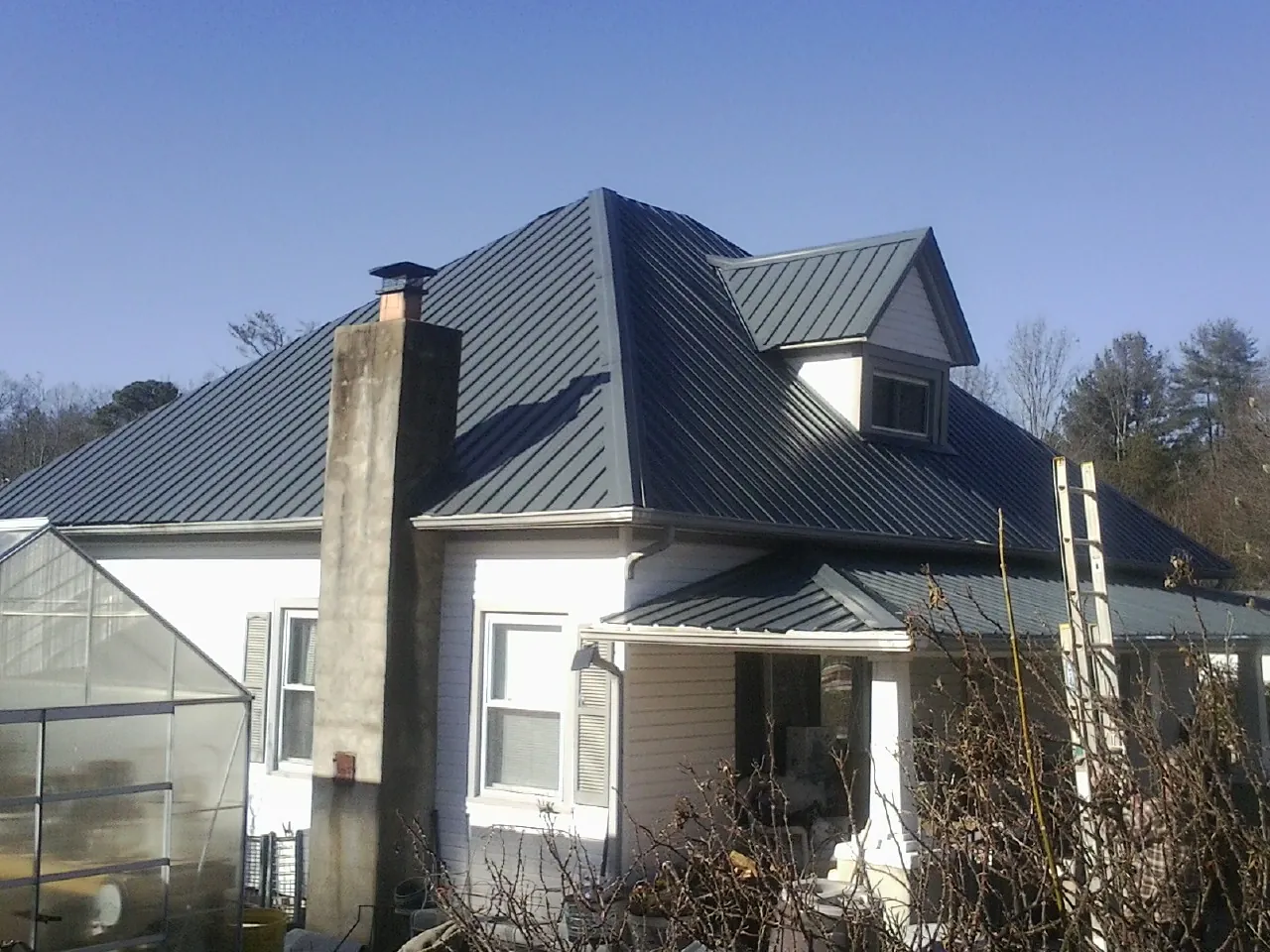 Dark blue standing seam metal roof on a white farmhouse with dormer — Slate & Tile Roof Repair by Roofing Brothers in West Ossipee
