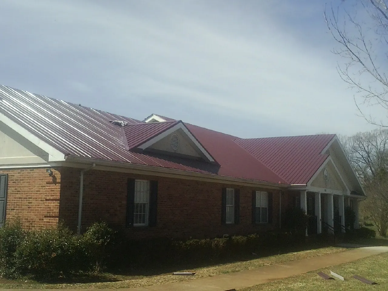 Red metal roof with gabled entries on a long brick building, from a Hail Damage Roof Repair job in West Ossipee