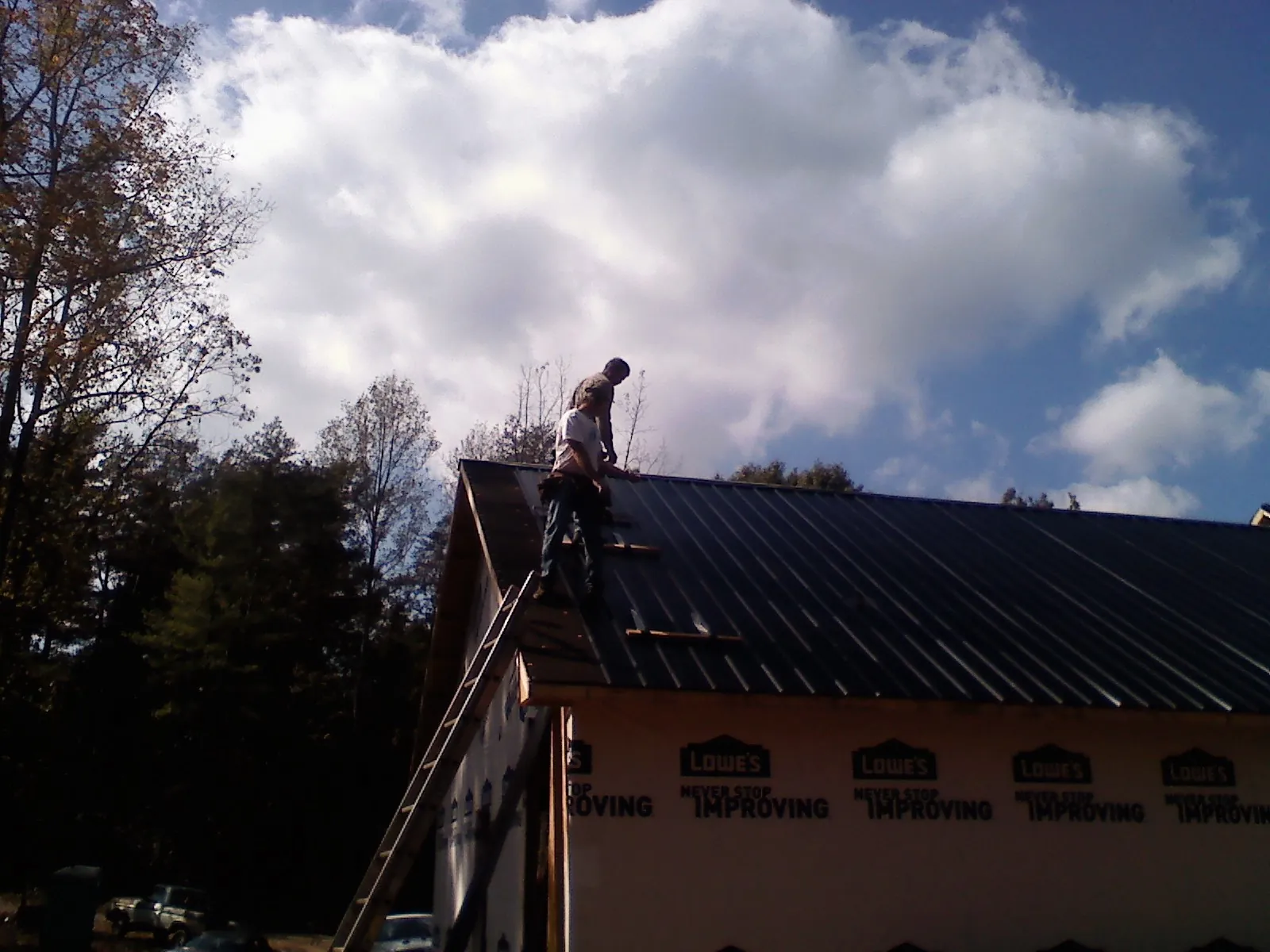 Roofer fastening dark metal panels high against a cloudy sky, from a Roof Inspection job in West Ossipee