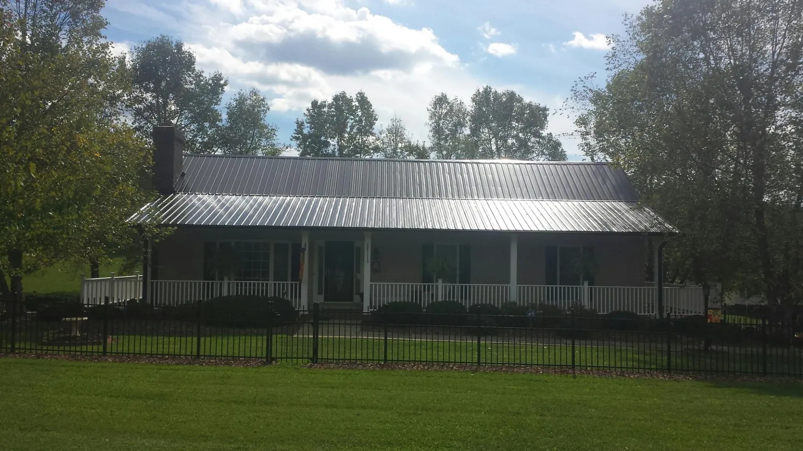 Gray metal roof on a brick ranch with a full width front porch — Gutter Guard Installation work by our crew in West Ossipee