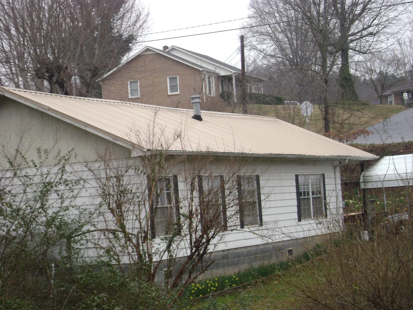 Tan metal roof on a white sided house set into a hillside — Commercial Roofing by Roofing Brothers in West Ossipee
