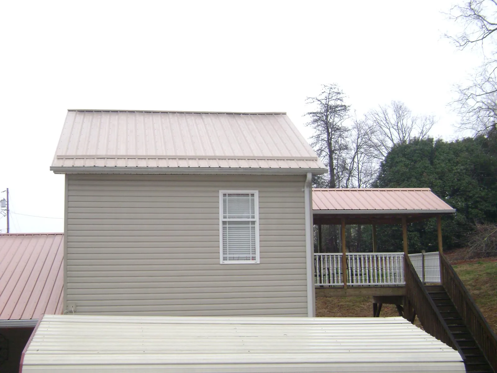 Tan metal roofs on a two story addition and attached porch, from a Roof Replacement job in West Ossipee